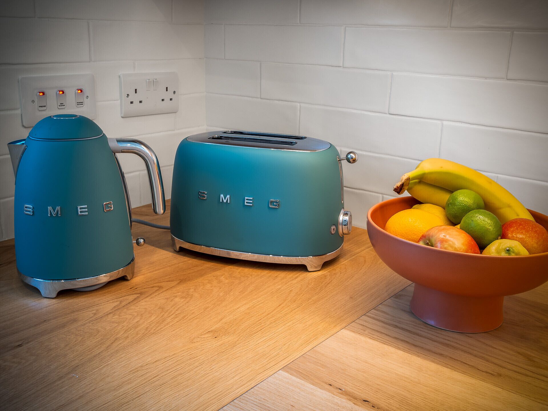 A kitchen with a toaster, kettle, and a bowl of fruit on the counter.