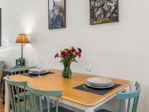 A dining area with a wooden table, two chairs, a vase with flowers, and two wine glasses. - The Old Forge Clifden (Clifden)