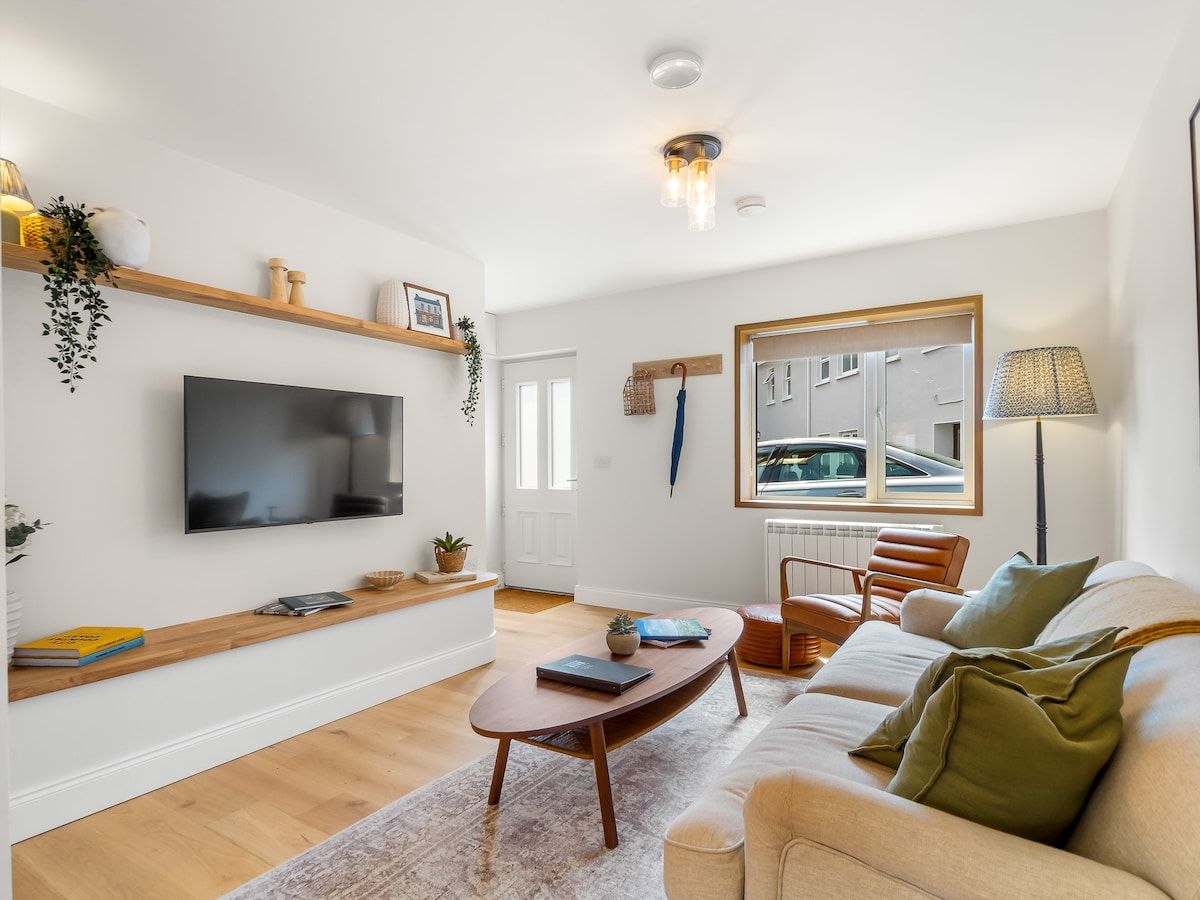 Ein modernes Wohnzimmer mit einem Flachbildfernseher, Holzregalen, einem Couchtisch, einer Couch und einem großen Fenster mit Blick auf ein Auto.