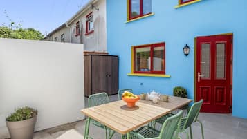 Eine Terrasse mit einem Holztisch und Stühlen, einer Obstschale und einer roter Tür.