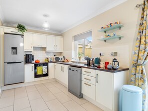 A modern kitchen with a dishwasher, oven, and refrigerator. There are shelves above the counter and a window providing natural light. - Cuirt Cregg Clifden (Clifden)