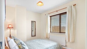 Une chambre à coucher avec un lit, une lampe de chevet, une fenêtre avec des stores et un radiateur.