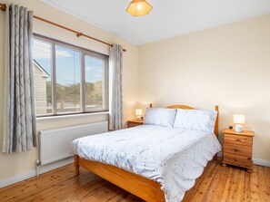Een slaapkamer met een houten bed, nachtkastjes met lampen, een raam met gordijnen en een radiator.