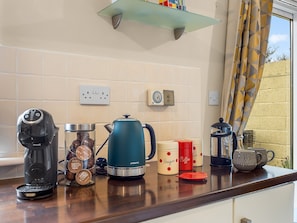 A kitchen counter with a coffee maker, a kettle, and coffee cups.