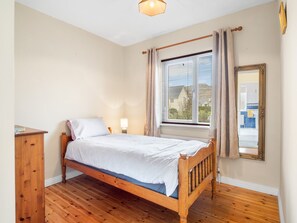 A single bed with a wooden frame, a bedside table, a lamp, and a window with curtains. - Cuirt Cregg Clifden (Clifden)