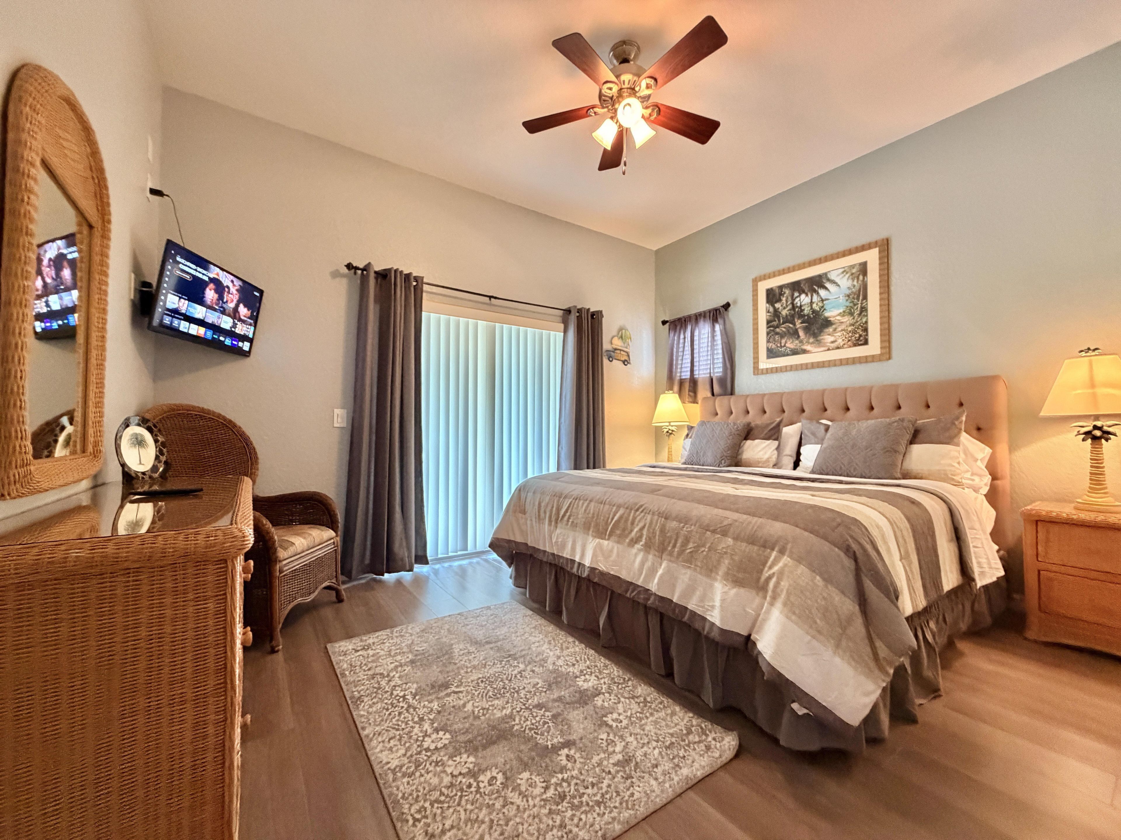 A bedroom with a bed, a ceiling fan, a TV, a window with curtains, a nightstand, and a lamp.