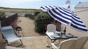 Un patio con una mesa lista para dos, una sombrilla a rayas y una silla.