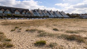 Una hilera de edificios modernos y angulares con techo plano, un primer plano arenoso y un cielo despejado.