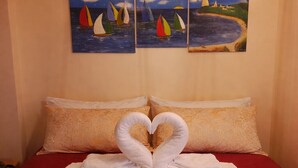 Una habitación de hotel con una cama, toallas con forma de corazón y dos cuadros de veleros.