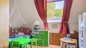 Un cuarto infantil con cama, escritorio verde y ventana con cortinas.