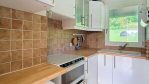 Una cocina con salpicadero de azulejos, encimera de madera, horno empotrado, armarios blancos y una ventana con vistas a zonas verdes.