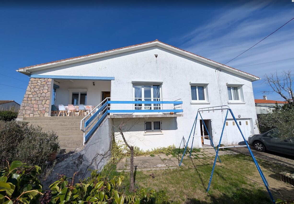 A two-story house with a stone facade, a balcony with blue railings, and a car parked in the driveway.