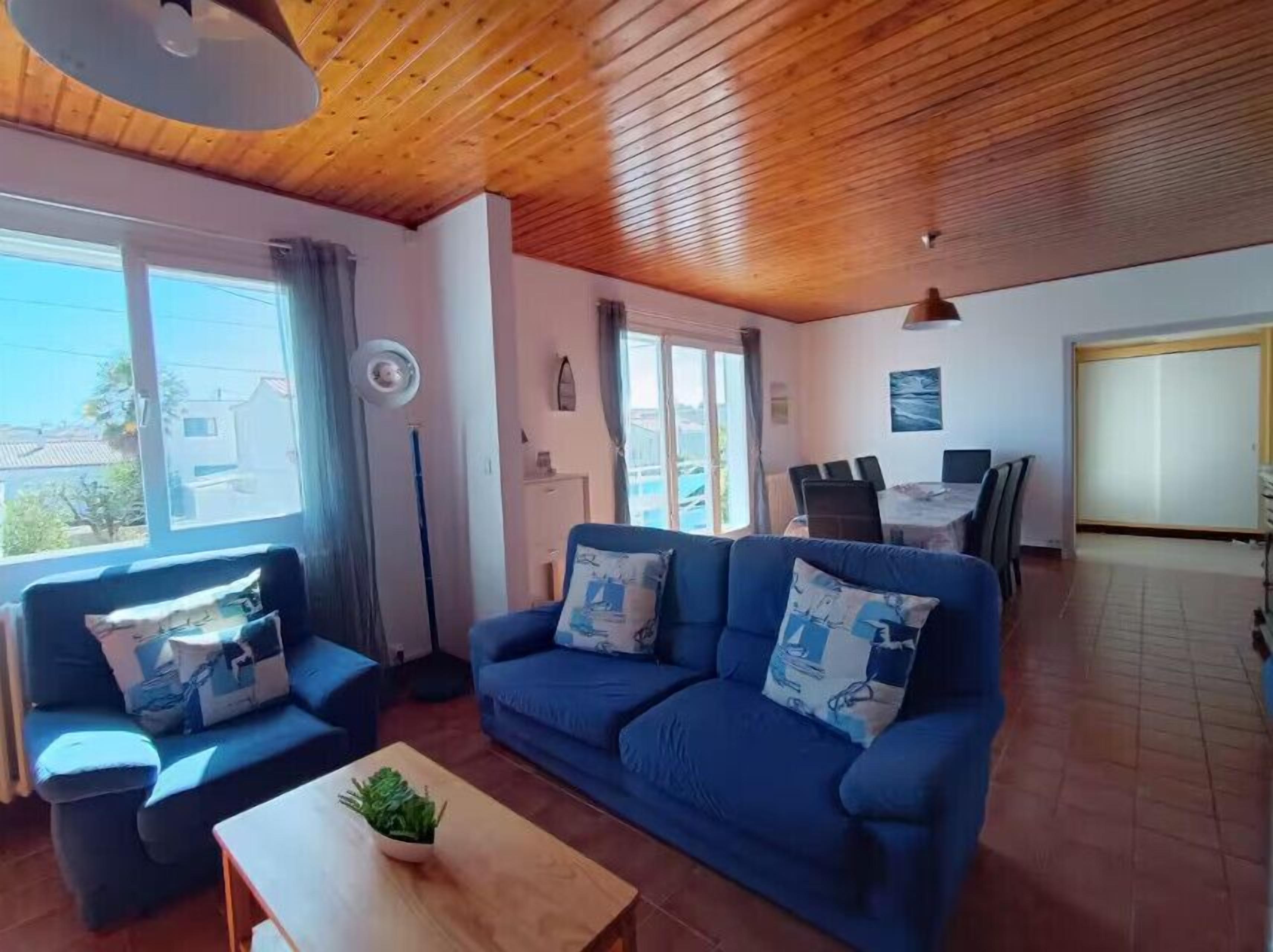 En stue med et blåt sofasæt, et træsofabord og et spiseområde med bord og stole.