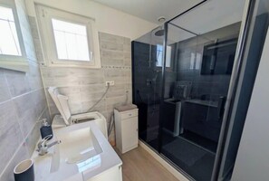 Un baño con cabina de ducha de vidrio, un lavabo, un inodoro y una ventana.