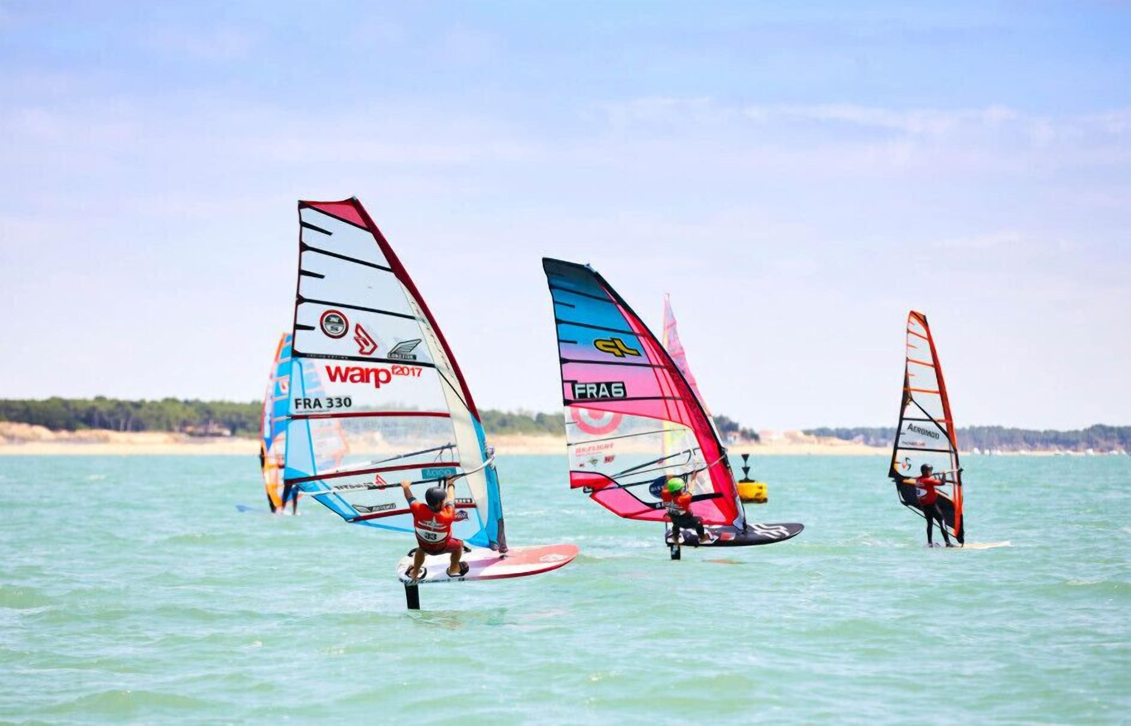 Tres windsurfistas en un cuerpo de agua bajo cielos despejados.