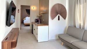 Ein kleines Hotelzimmer mit Bett, Küchenzeile, Sofa, Fernseher und einem dekorativen Ventilator.