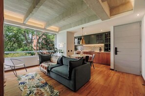 Ein modernes Wohnzimmer mit Sofa, einem Esstisch und einer dahinterliegenden Küche.