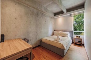 Ein Schlafzimmer mit Bett, einem Holztisch und einem Fenster mit Blick auf Bäume.