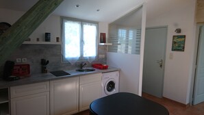 Eine kleine Küche mit Waschmaschine, einem Fenster mit Jalousien und einer Tür mit Schild.