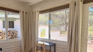 A room with a bed, a desk, and a chair, with a window offering a view of a building and trees.