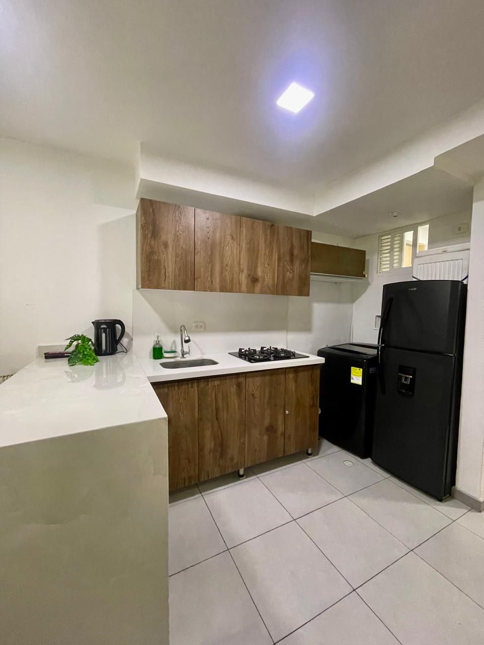 A compact kitchen with white countertops, wooden cabinets, a black refrigerator, and a gas stove.