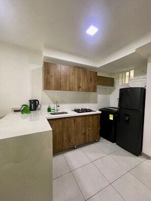 A compact kitchen with white countertops, wooden cabinets, a black refrigerator, and a gas stove. - Sunset47 sea and life (Cartagena de Indias)