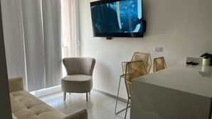 Un salon moderne avec un téléviseur à écran plat fixé au mur, un canapé, deux fauteuils et une table à manger.