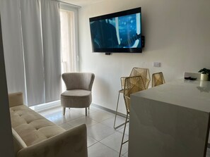 Ein modernes Wohnzimmer mit einem flachbildfernseher an der Wand, einem Sofa, zwei Sesseln und einem Esstisch.