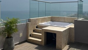 Une terrasse sur le toit avec un jacuzzi, une plante en pot et une vue sur la ville.