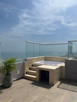Eine Dachterrasse mit Whirlpool, einer Topfpflanze und Blick auf die Stadt.