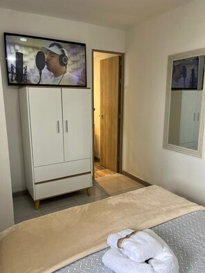 A bedroom with a bed, a wardrobe, a mirror, and a television displaying a person with headphones. - Sunset47 sea and life (Cartagena de Indias)