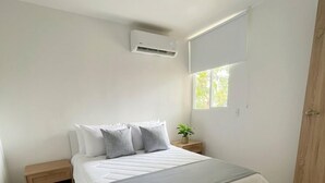 Une chambre à coucher comprenant un lit, une table de chevet, une fenêtre et un appareil de climatisation.