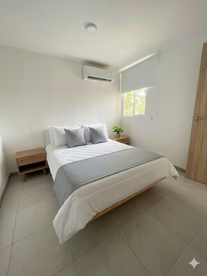 Ein Schlafzimmer mit einem Bett, einem Nachttisch, einem Fenster und einer Klimaanlage.