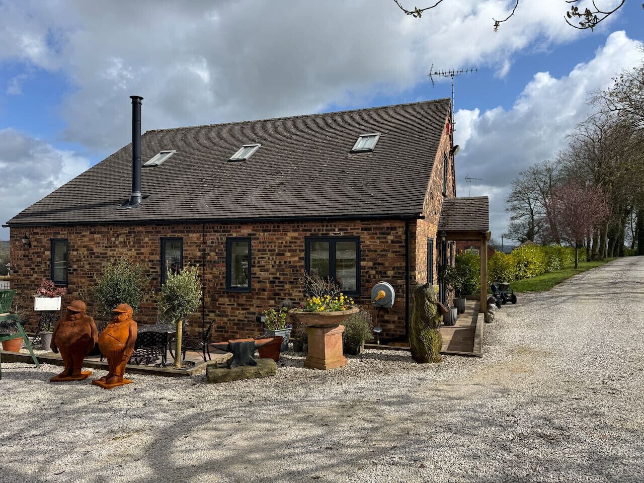 A brick building with a sloped roof, a chimney, and a gravel driveway.