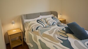 Un letto rifatto con lenzuola a fantasia, due comodini con lampade e un piccolo tavolo in legno.