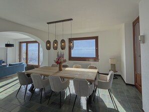 A dining area with a large wooden table, six chairs, hanging pendant lights, and a vase of flowers. - Comfortable lakefront family apartment (GERA LARIO)