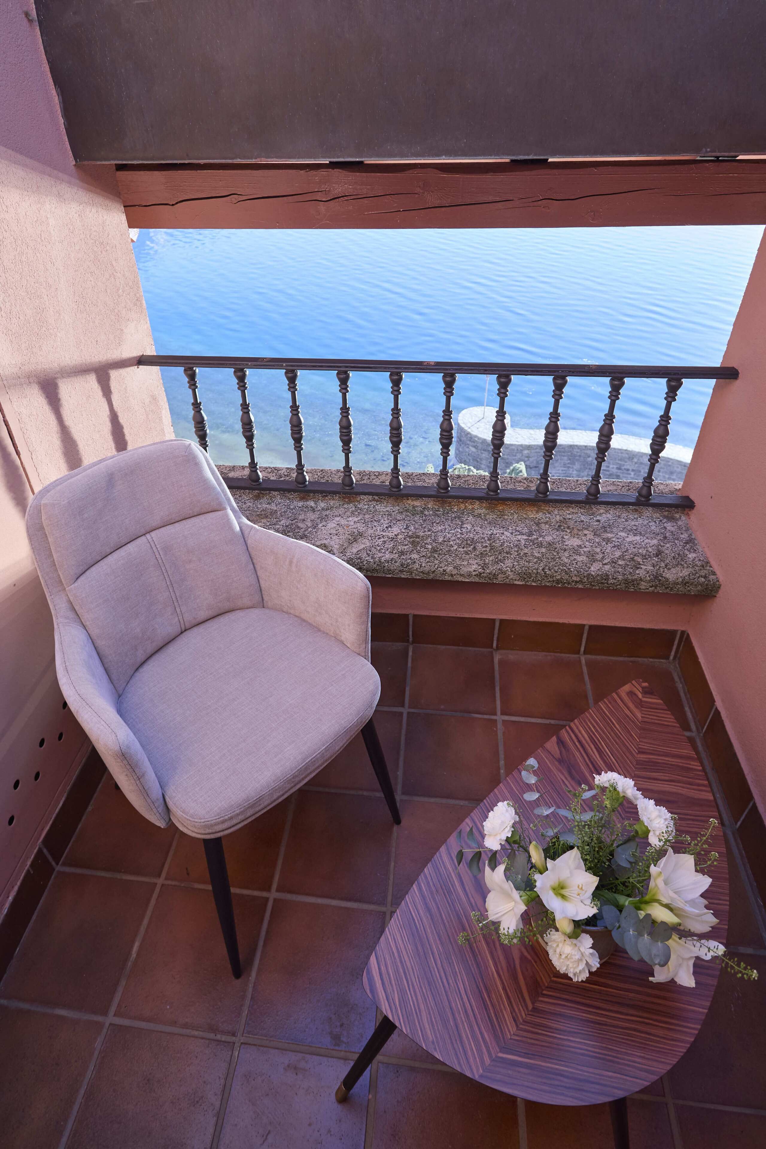 A balcony with a chair and a table with a floral arrangement.
