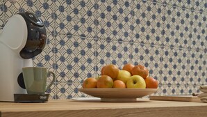 Una cocina con cafetera, un plato de fruta y un enfriador de vino con botellas.