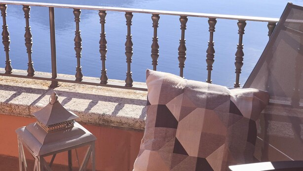 Un balcón con vistas al mar, una silla, un cojín y un farol.