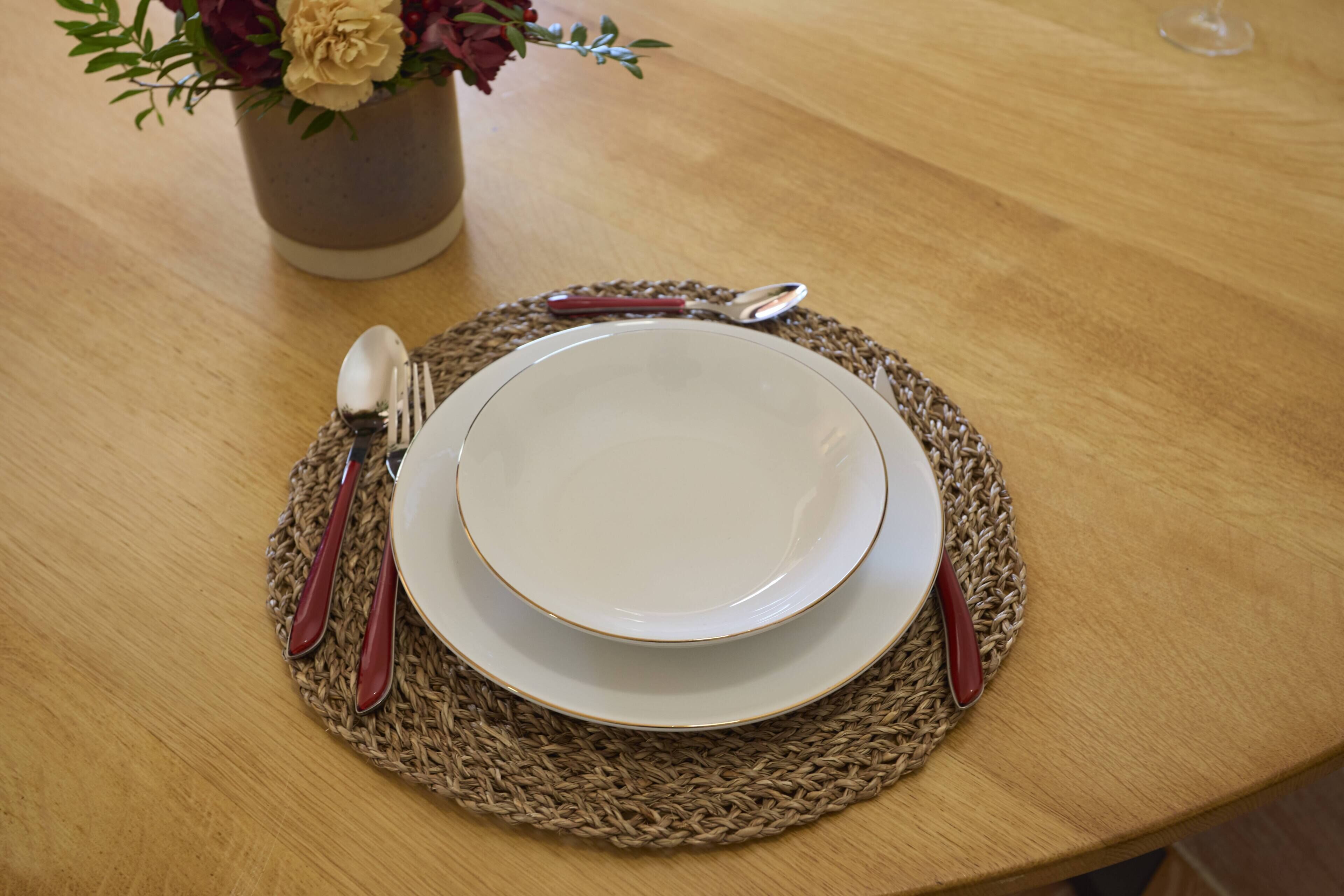 Une table dressée avec une assiette, un bol, une cuillère et une fourchette, le tout posé sur un set de table en fibres tressées.