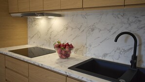 Una cucina con mobili in legno, zoccolo in marmo, rubinetto nero e una ciotola di frutta sul piano di lavoro.