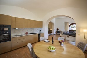 A modern kitchen with wooden cabinets, a marble countertop, and a dining area with a round table and chairs. - Charming apartment - ground floor (GERA LARIO)