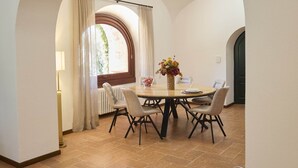 Zona pranzo con tavolo rotondo, sedie, un vaso di fiori e una finestra con tende.