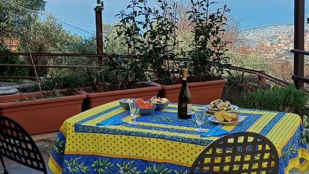 A table set outdoors with a view of a city and mountains in the background. - A large terrace overlooking the sea in the quiet of olive trees for families (Santa Giulia)