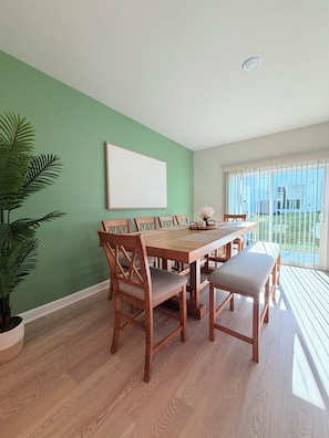 Un comedor con una mesa y sillas de madera, una pared verde y una ventana con vistas al exterior.