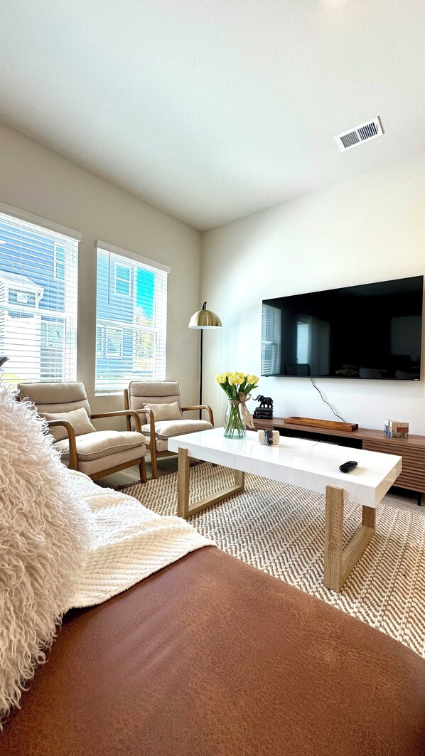 Una sala de estar moderna con un sofá, dos sillones, una mesa de centro, un televisor y un jarrón con flores.
