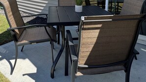 Eine Terrasse mit Tisch und Stühlen, einem Blumentopf sowie ein Haus mit großen Fenstern und einer Tür.