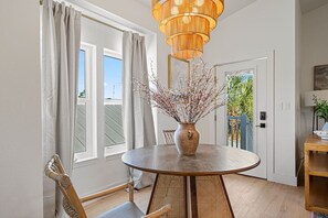 A dining area with a round table, wicker chairs, a vase with branches, and a wooden ceiling light fixture. - 12BDR Luxury Estate For Large Groups (Destin)