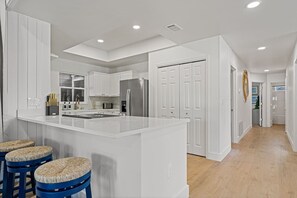 A modern kitchen with white cabinetry, a central island, and a bar area with stools. - 12BDR Luxury Estate For Large Groups (Destin)