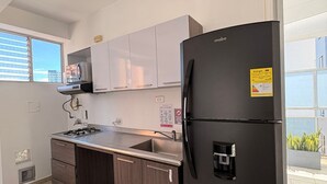 A modern kitchen with a black refrigerator, grey cabinets, a stainless steel sink, and a window with blinds.